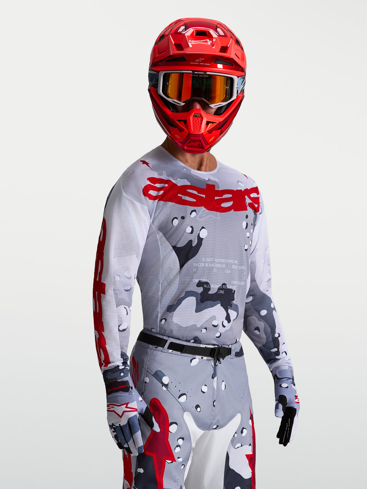 Maillot Racer Air Lone, maillot de motocross pour homme, gris camouflage et rouge vif, en mesh respirant pour temps chaud, porté par un pilote avec un casque.