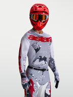 Maillot Racer Air Lone, maillot de motocross pour homme, gris camouflage et rouge vif, en mesh respirant pour temps chaud, porté par un pilote avec un casque.