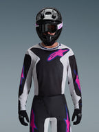 Maillot Alpinestars Fluid Grid 2026, maillot de motocross, noir, gris clair et violet, porté par un pilote avec un pantalon tout-terrain assorti, un casque noir et des lunettes, tenue de course haute performance complète