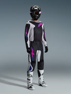 Ensemble d'équipement Alpinestars 2026 Fluid Grid, pilote de motocross portant un maillot et un pantalon noir et blanc avec des accents roses et bleus, casque noir, gants noirs et bottes blanches, tenue de course complète sur un fond gris