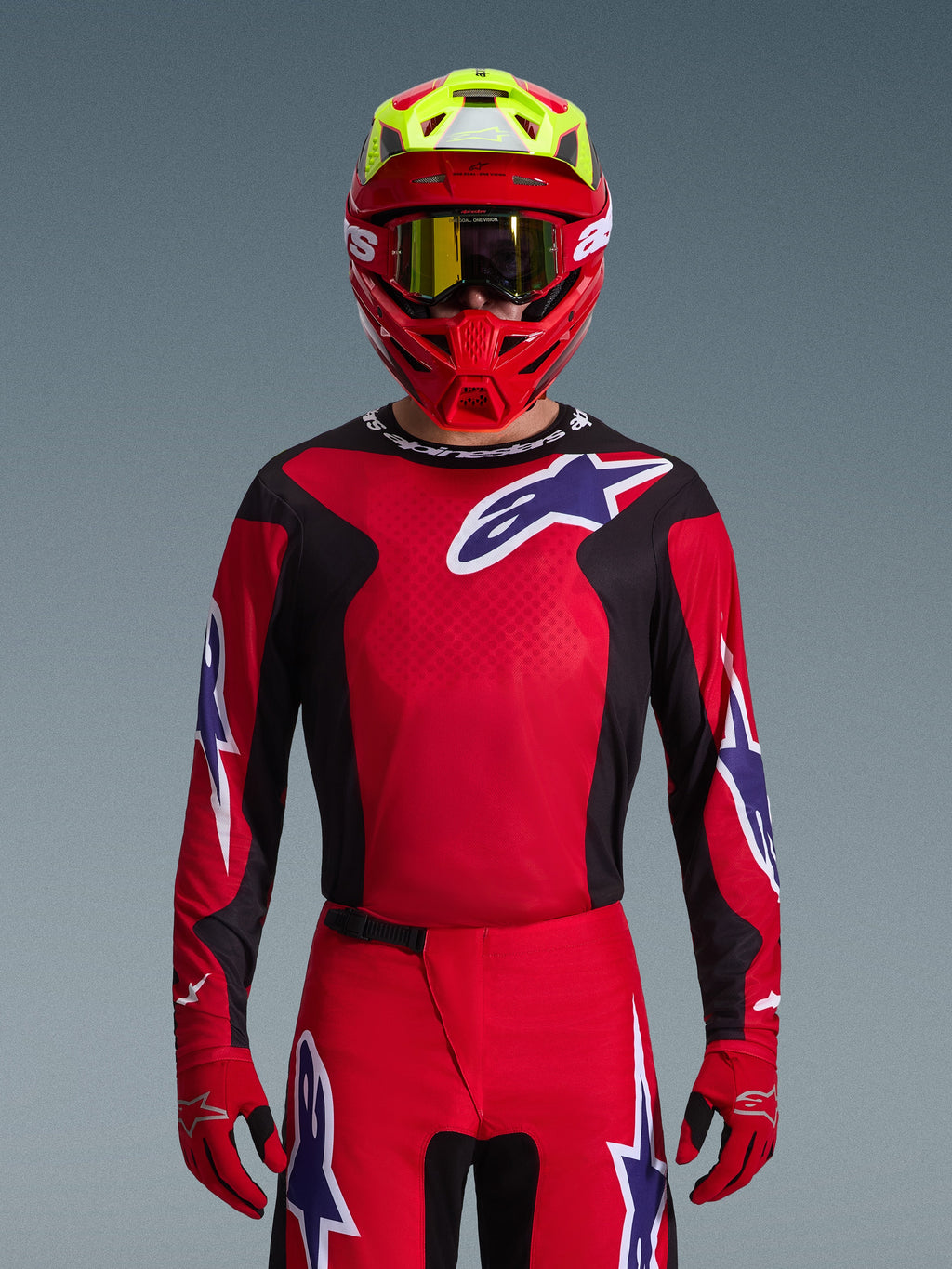 Pilote de motocross portant l'ensemble d'équipement Alpinestars 2026 Fluid Grid, maillot rouge avec empiècements latéraux noirs et logo étoile blanc, pantalon et gants rouges assortis, casque rouge et jaune avec lunettes à écran teinté doré, équipement de course haute performance pour le tout-terrain