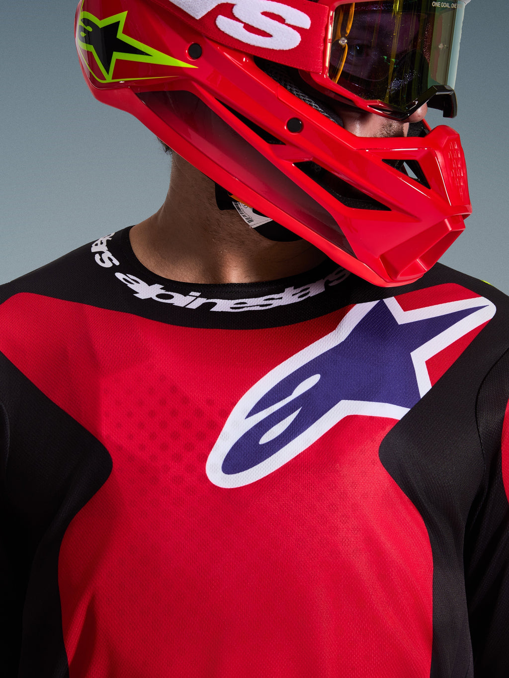 Maillot Alpinestars Fluid Grid 2026, rouge, noir et violet, pilote de motocross portant le maillot avec un casque et des lunettes rouges assortis, large logo blanc et violet sur la poitrine, col sport avec marquage Alpinestars, équipement technique de course tout-terrain