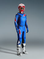 Pilote de motocross portant le maillot Alpinestars 2026 Fluid Grid en Bleu Rouge, avec pantalon de motocross assorti, bottes blanches et noires, et casque rouge et blanc, ensemble d'équipement professionnel pour la performance tout-terrain