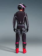Pilote de motocross vu de dos portant le maillot Alpinestars Fluid Apex 2026 et le pantalon assorti Noir/Gris, avec des lignes géométriques blanches et des logos étoiles sur l'assise, accompagné d'un casque noir et rose et de bottes de course rouges et noires.
