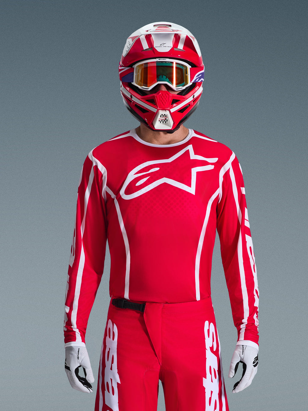 Motocross rider wearing complete Alpinestars 2026 Fluid Apex Gear Set, red jersey with large white star logo on the chest, matching red pants with white branding, red and white helmet with iridescent goggles, white and black gloves, coordinated red and white outfit for off-road racing