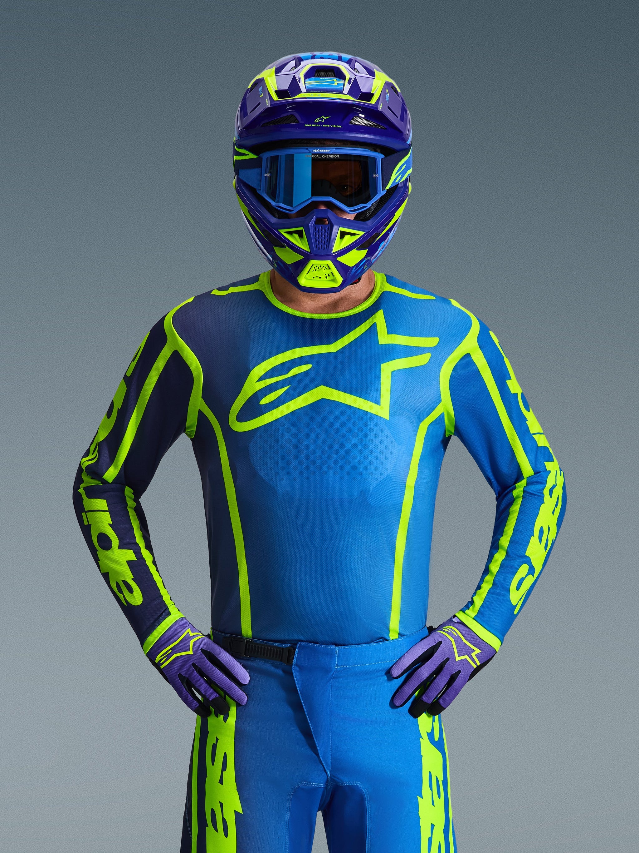 Pilote de motocross portant le maillot Alpinestars 2026 Fluid Apex en coloris Blue Yellow Fluo, doté d'une base bleu vif avec des motifs jaune fluo et un grand logo sur la poitrine, coordonné avec un casque et des gants assortis, conçu pour le tout-terrain et le motocross.