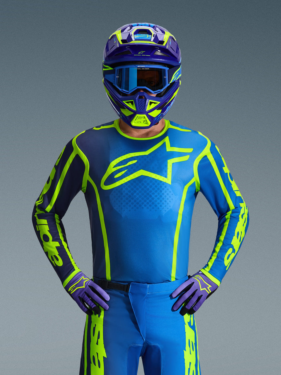 Pilote de motocross portant le maillot Alpinestars 2026 Fluid Apex en coloris Blue Yellow Fluo, doté d'une base bleu vif avec des motifs jaune fluo et un grand logo sur la poitrine, coordonné avec un casque et des gants assortis, conçu pour le tout-terrain et le motocross.