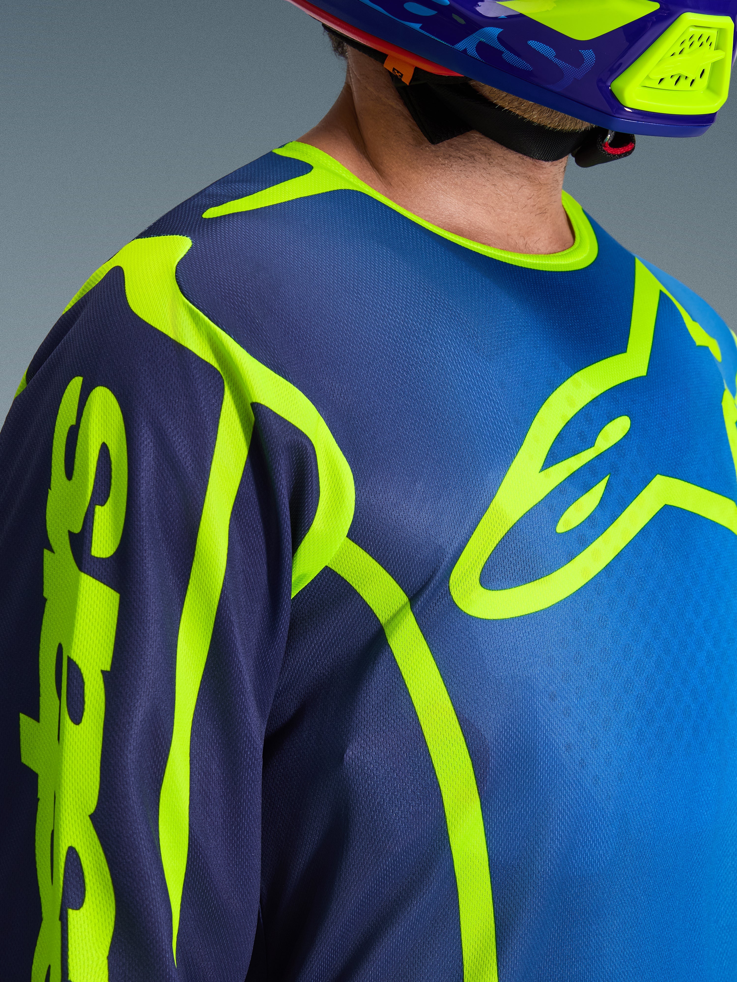 Close-up of the Alpinestars 2026 Fluid Apex Jersey in Blue and Yellow Fluo, featuring a large neon yellow Astars logo on the chest, matching motocross helmet, moisture-wicking polyfabric construction.