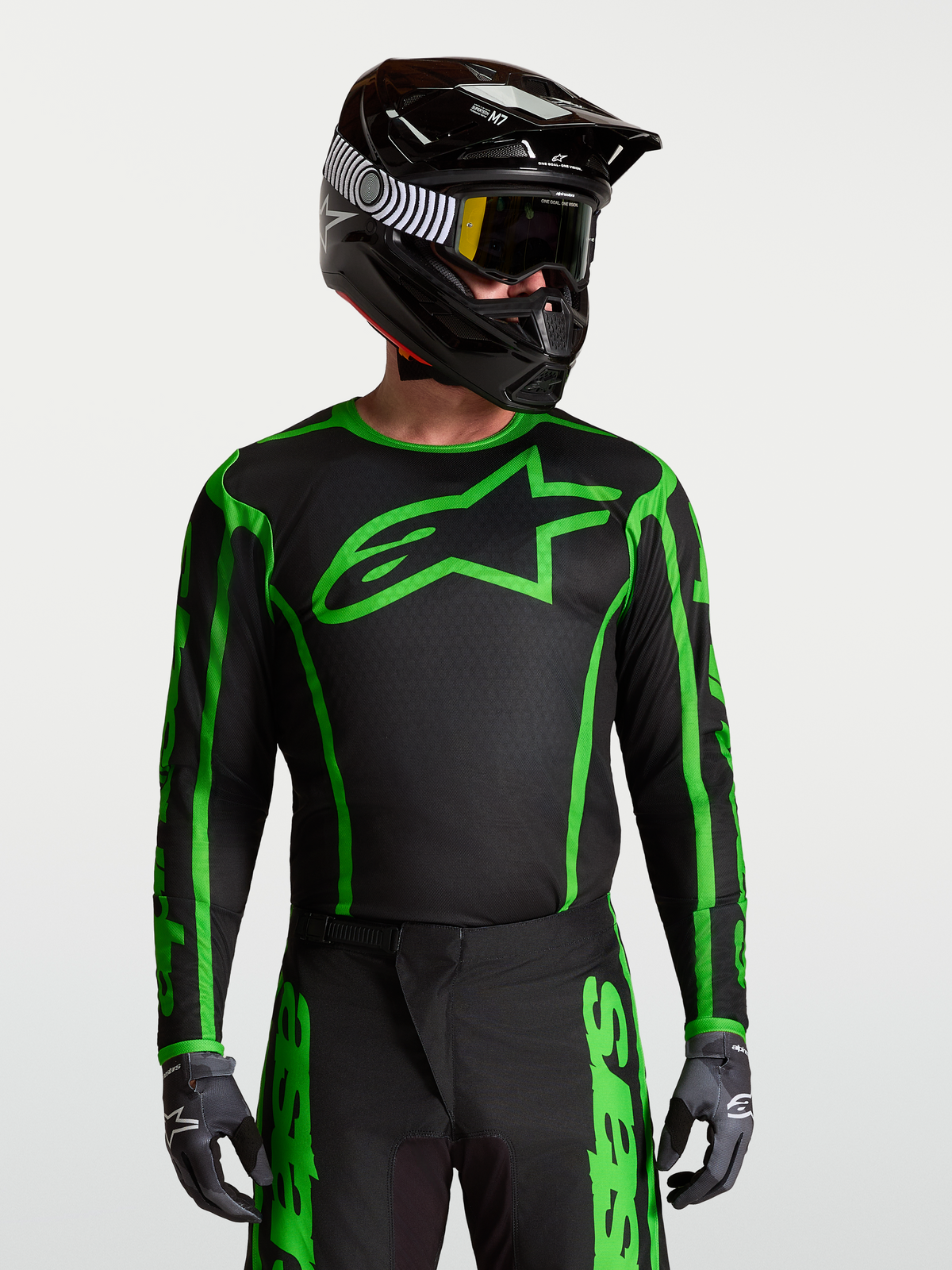 Maillot Alpinestars Fluid Apex V2, maillot de motocross noir et vert fluo en poly-tissu respirant porté avec un casque de protection.