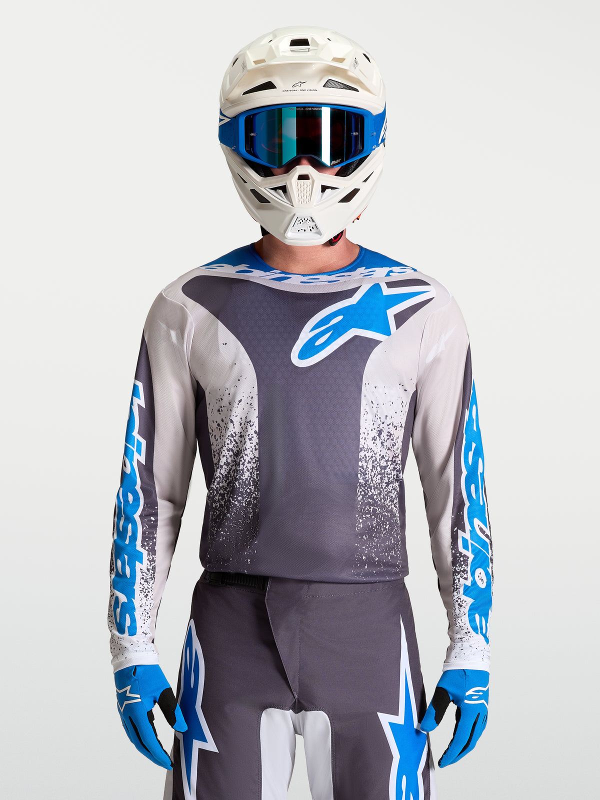 Maillot Fluid Drag Alpinestars, maillot de motocross pour homme, gris et bleu, construction légère et respirante, porté avec casque et gants assortis, équipement tout-terrain haute performance