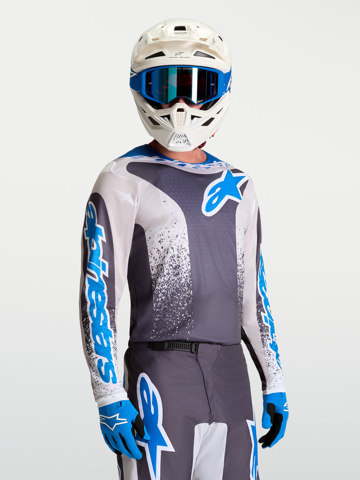 Maillot Alpinestars Fluid Drag, maillot de motocross performant gris et bleu porté avec un casque et des gants blancs.