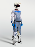 Maillot Racer Amber Alpinestars, tenue de motocross pour homme, gris cendré et bleu, porté par un mannequin avec casque et bottes de performance.