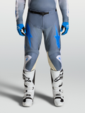 Alpinestars pantalon Racer Amber 2027, motocross pour homme, gris et bleu, porté avec des bottes blanches.