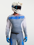 Alpinestars Maillot Racer Amber, maillot de motocross pour homme, gris et bleu, porté avec casque et masque blancs, équipement tout-terrain haute performance