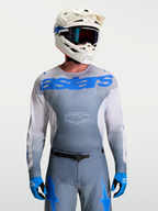 Alpinestars Maillot Racer Amber, maillot de motocross pour homme, gris et bleu, porté avec casque et masque blancs, équipement tout-terrain haute performance