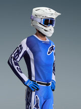 Maillot Alpinestars 2026 Racer Air Portl, maillot de motocross, bleu UCLA et blanc, porté avec un casque blanc, des lunettes bleues et des gants assortis, conception en maille respirante pour les courses tout-terrain par fortes chaleurs.