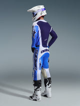Pilote de motocross vu de dos portant le maillot Alpinestars 2026 Racer Air Portl en bleu Ucla et blanc, associé à un pantalon de motocross assorti, un casque Supertech blanc et des bottes blanches, présentant un ensemble d'équipement de course complet et coordonné.