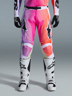 Alpinestars 2026 Racer Air Portl Pants, pantalon de motocross, dégradé vibrant de violet, rose et orange, avec des logos d'étoiles sur les cuisses, porté avec des bottes de course blanches et des gants noirs, conçu pour la conduite tout-terrain haute performance