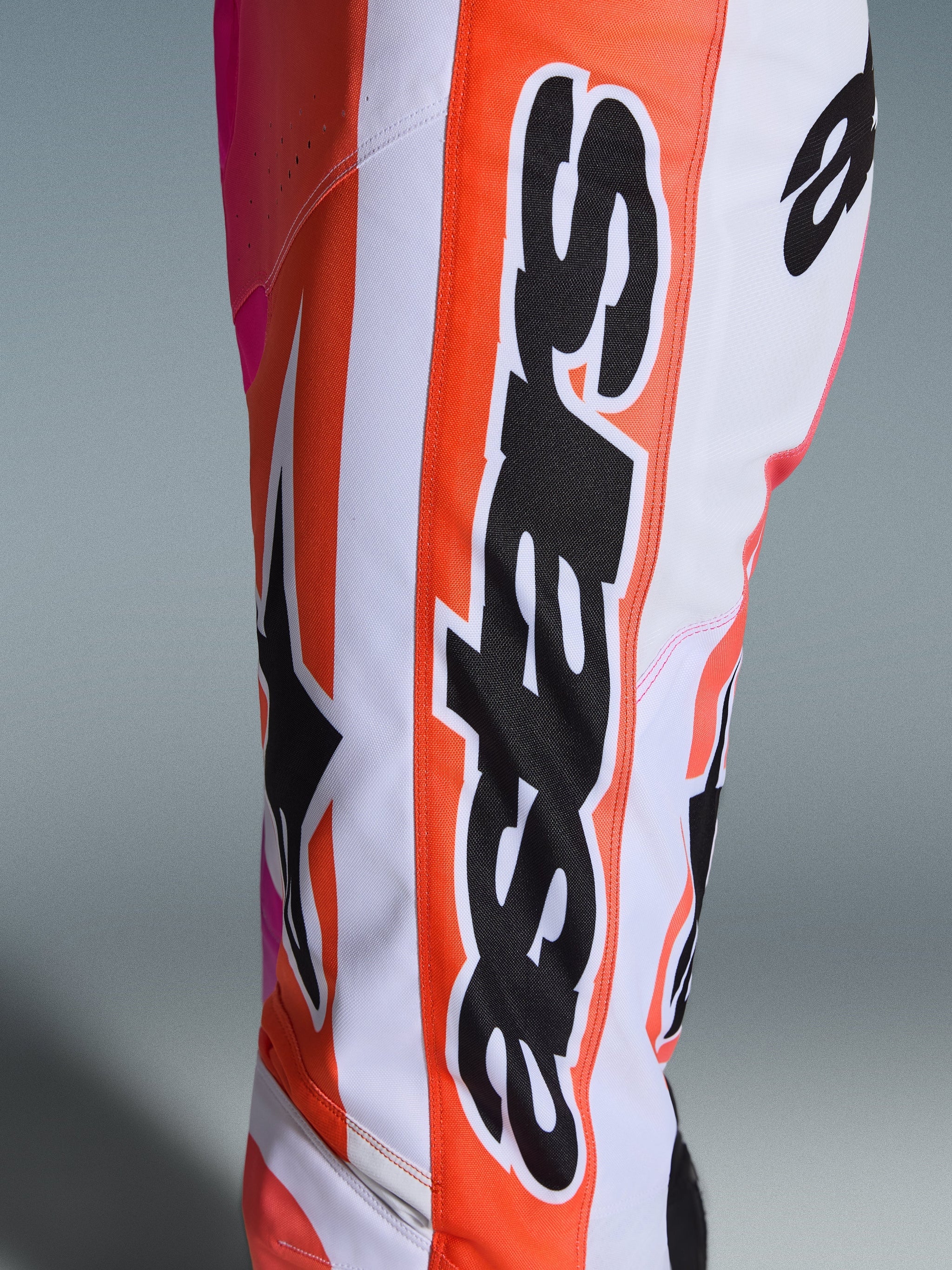 Pantalon Alpinestars Racer Air Portl 2026, pantalon de motocross, orange, blanc et rose, gros plan sur le marquage Alpinestars noir et le logo étoile, tissu perforé pour la ventilation, équipement de course tout-terrain durable