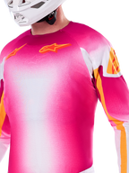 Maillot Alpinestars Édition Limitée Supertech AFD MIG, maillot de motocross avec dégradé rose fluo et blanc, logos Astars orange et accents sur les manches, porté par un pilote avec un casque blanc, coupe de course athlétique