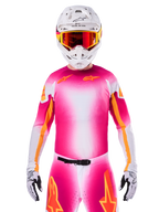 Alpinestars Limited Edition Supertech AFD MIG Jersey, maillot de motocross rose fluo et blanc, avec un dégradé éclatant et des logos d'étoiles orange, porté comme une tenue de course complète avec pantalon assorti, casque blanc et lunettes rouges, équipement professionnel pour le tout-terrain