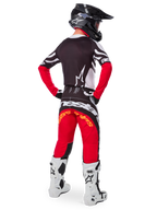 Vue arrière d'un pilote de motocross portant l'ensemble Techstar Deep Édition Limitée d'Alpinestars, comprenant un maillot noir avec des accents blancs et rouges, un pantalon rouge et noir assorti avec logo Alpinestars, des bottes de course blanches et un casque noir, présentant la tenue de course tout-terrain complète.