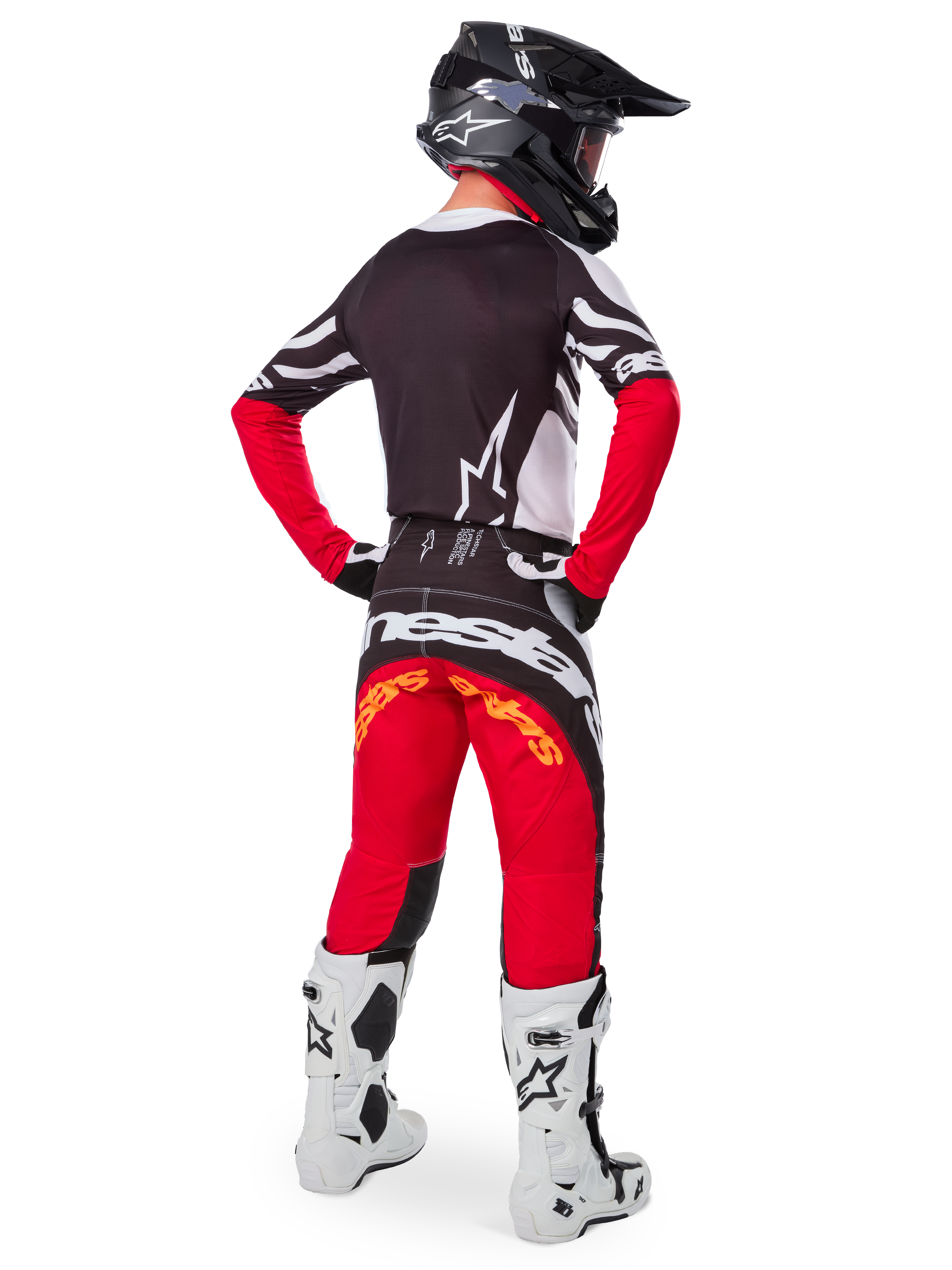 Pilote de motocross vu de dos portant le maillot Alpinestars Limited Edition Techstar Deep en Noir Blanc Rouge Intense, avec un dos noir orné d'un logo étoile blanc et des manches rouges, associé à un pantalon assorti rouge et noir, des bottes blanches et noires et un casque noir pour une tenue complète de course tout-terrain.