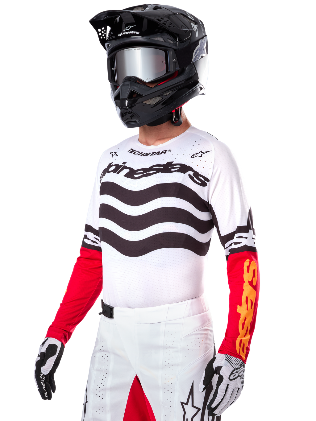 Pilote de motocross portant le maillot Alpinestars Limited Edition Techstar Deep, maillot blanc avec rayures ondulées noires et bas de manches rouges, assorti à un casque noir, des lunettes miroir, des gants blancs et noirs et un pantalon de course blanc, tenue de motocross haute performance.