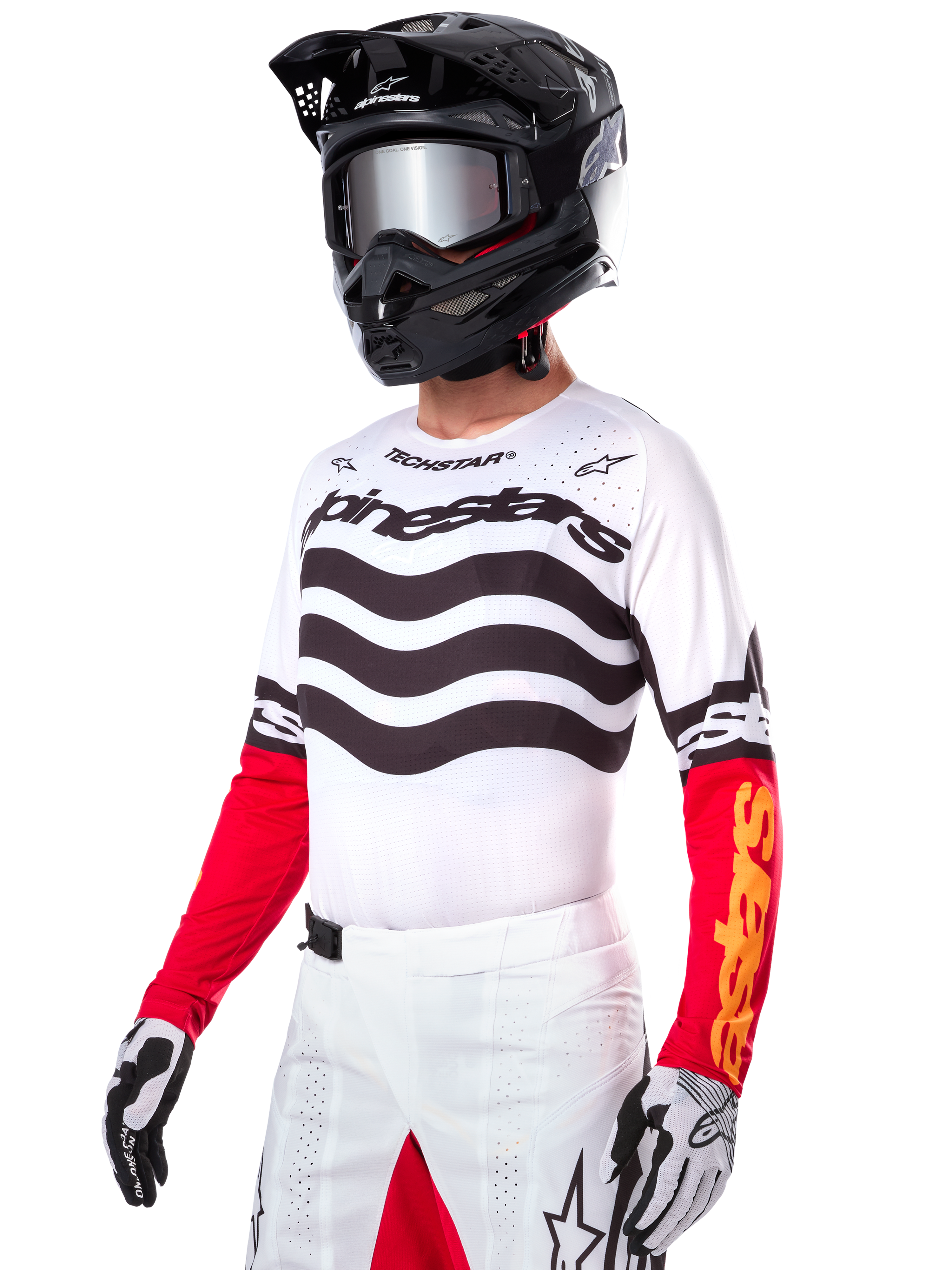 Pilote de motocross portant le maillot Alpinestars Limited Edition Techstar Deep, maillot blanc avec rayures ondulées noires et bas de manches rouges, assorti à un casque noir, des lunettes miroir, des gants blancs et noirs et un pantalon de course blanc, tenue de motocross haute performance.