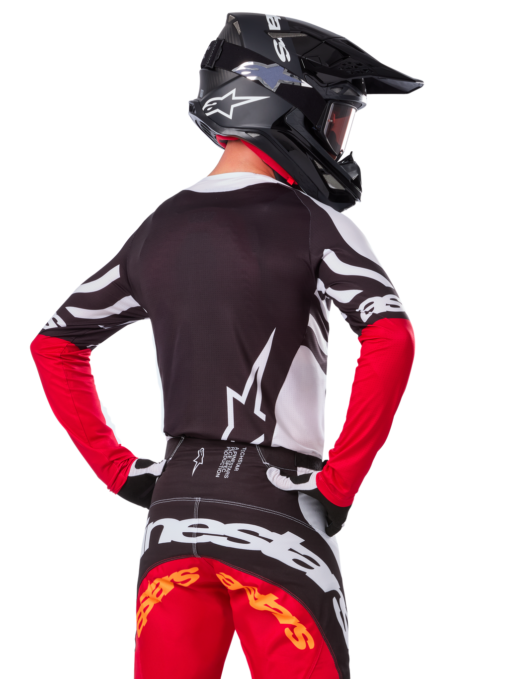 Pilote de motocross vu de dos portant le maillot Alpinestars Limited Edition Techstar Deep, noir, blanc et rouge vif, avec un pantalon de course assorti et un casque noir, coupe athlétique pour la performance tout-terrain