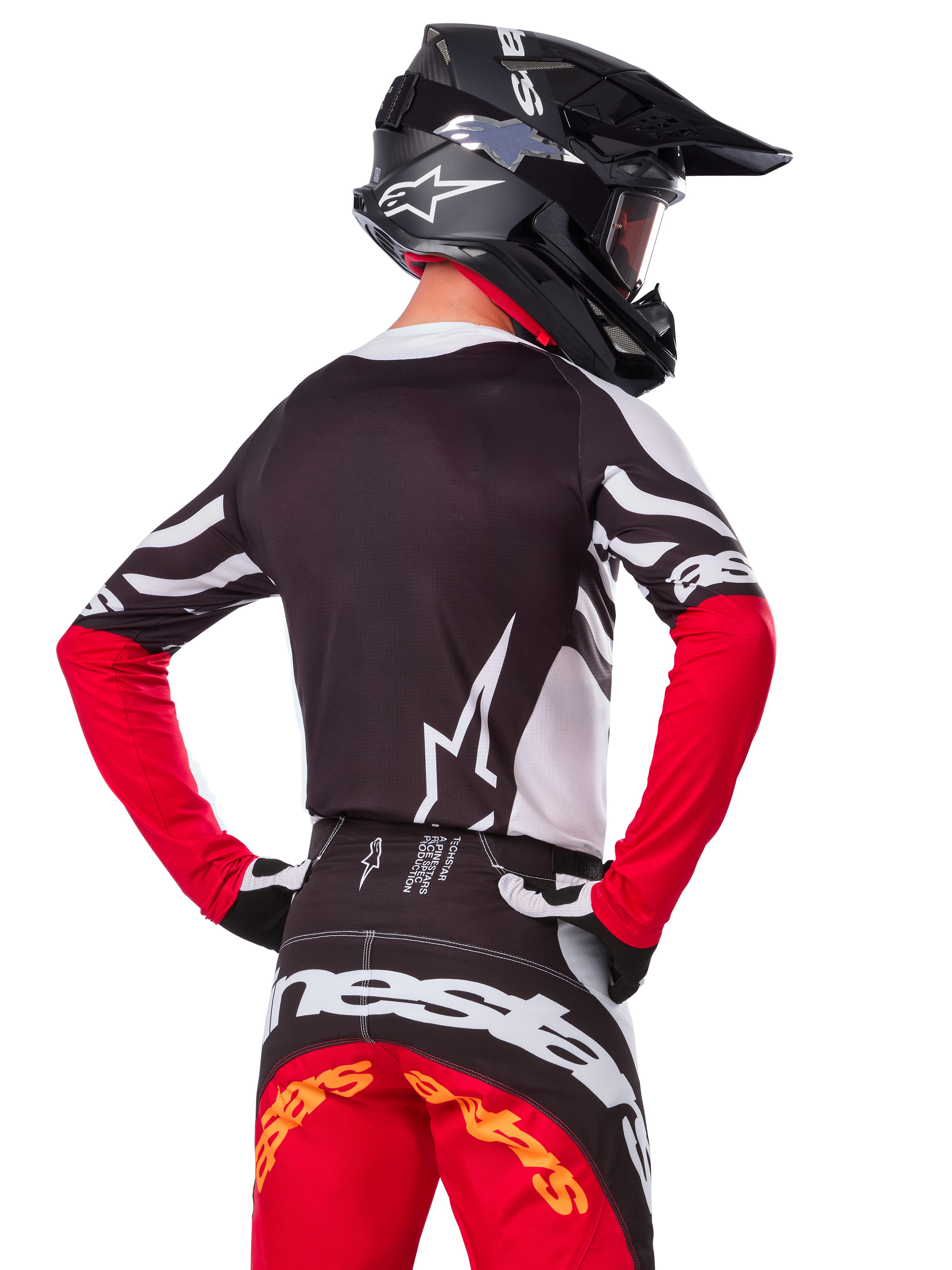 Pilote de motocross en tenue de course complète Alpinestars, Maillot Techstar Deep Édition Limitée noir, blanc et rouge vif, vue de dos, pantalon Techstar Deep assorti, casque noir avec masque, gants noirs et blancs, tenue de course tout-terrain professionnelle