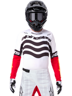 Pilote de motocross en tenue de course complète, Maillot Techstar Deep Édition Limitée blanc et noir avec manches rouges, graphismes ondulés et logo Alpinestars distinctif, pantalon de motocross blanc, casque et lunettes noirs, tenue coordonnée pour la course tout-terrain