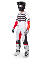 Pilote de motocross portant un équipement de course complet, Maillot Techstar Deep Limited Edition avec des rayures ondulées blanches et noires et des manches rouges, pantalon blanc et rouge assorti, casque noir, bottes blanches et noires, tenue coordonnée pour la course tout-terrain