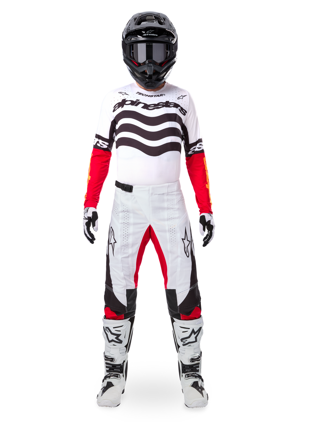 Pilote de motocross portant l'ensemble d'équipement Alpinestars Techstar Deep Édition Limitée, maillot blanc avec graphismes de vagues noirs et manches rouges, pantalon blanc et noir assorti avec accents rouges à l'intérieur des cuisses, casque noir avec lunettes sombres et bottes blanches, tenue de course tout-terrain professionnelle complète