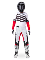 Pilote de motocross portant l'ensemble d'équipement Alpinestars Techstar Deep Édition Limitée, maillot blanc avec graphismes de vagues noirs et manches rouges, pantalon blanc et noir assorti avec accents rouges à l'intérieur des cuisses, casque noir avec lunettes sombres et bottes blanches, tenue de course tout-terrain professionnelle complète