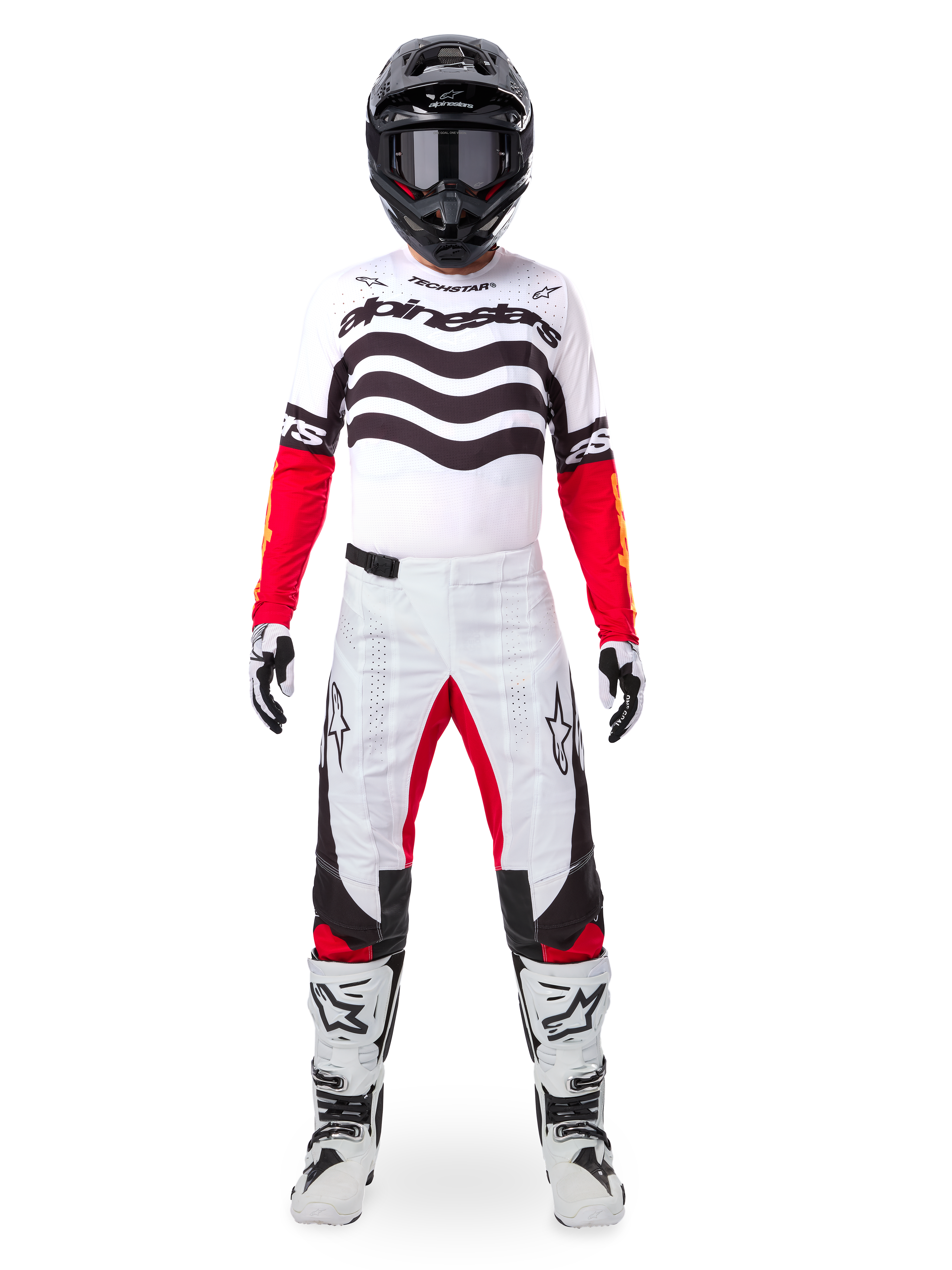 Pilote de motocross portant le maillot Alpinestars Techstar Deep Édition Limitée en blanc, noir et rouge, avec des graphismes ondulés sur la poitrine, associé à un pantalon blanc et rouge assorti, un casque noir et des bottes de course blanches, tenue de motocross professionnelle complète.