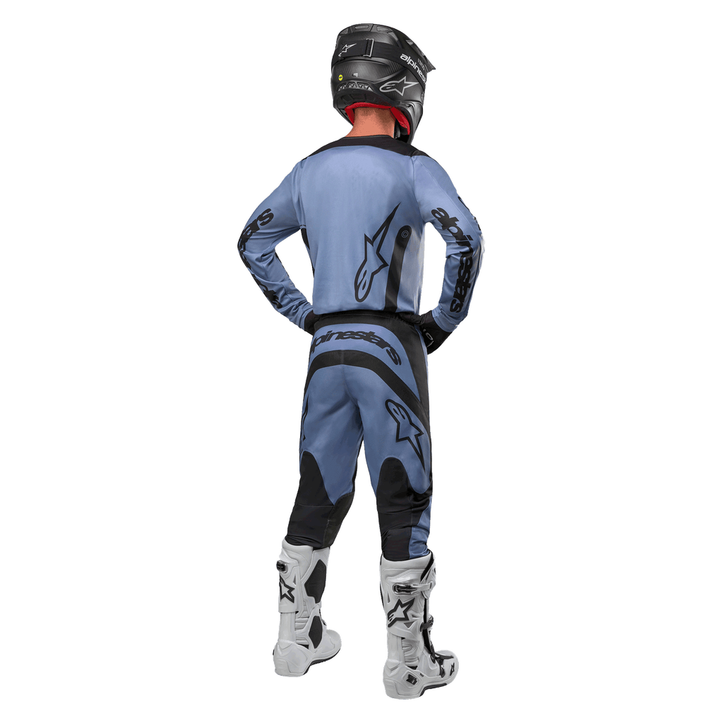 Pilote de motocross de dos portant le maillot Alpinestars 2024 Fluid Lurv et le pantalon assorti bleu clair et noir, avec logos noirs sur le dos et les manches, associé à un casque noir et des bottes blanches.