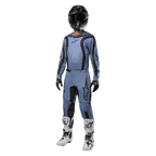 Pilote de motocross portant un équipement de course complet, maillot Alpinestars Fluid Lurv 2024 bleu clair et noir, pantalon bleu clair assorti avec empiècements noirs, bottes blanches et noires, gants noirs et casque noir avec lunettes, tenue coordonnée pour la course tout-terrain