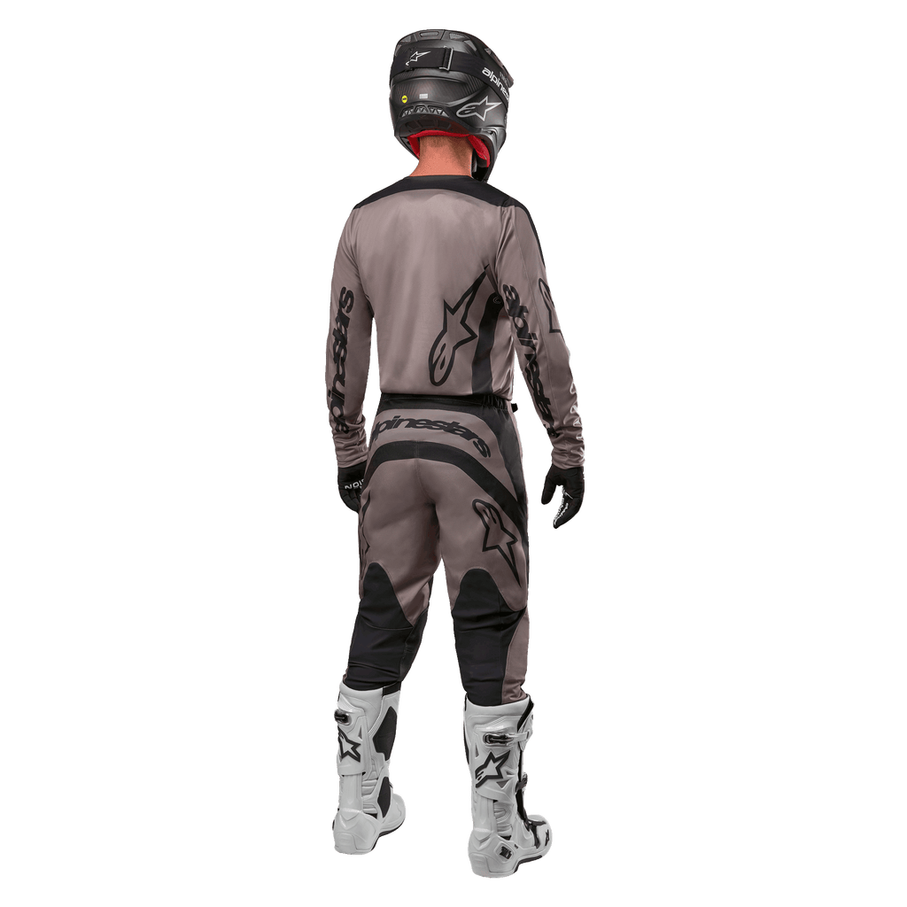 Alpinestars 2024 Fluid Lurv Jersey, Motocross Jersey, Mud Black, rear view of motocross rider wearing matching racing gear, black helmet, and white boots, featuring bold black Alpinestars logos and an athletic fit for off-road performance.