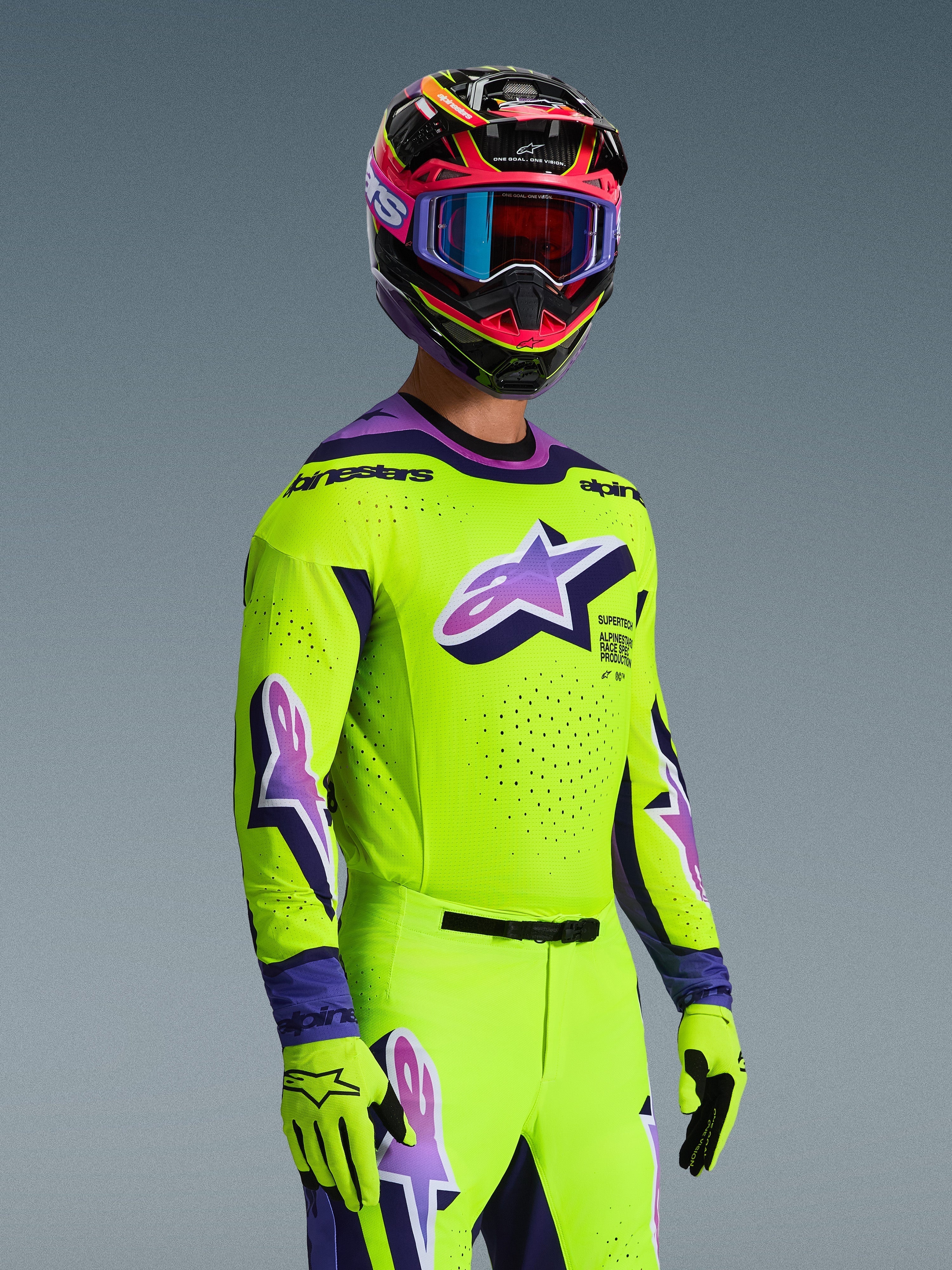 Pilote de motocross portant le maillot Alpinestars 2026 Supertech Vista, jaune vif avec des accents violets et noirs, pantalon et gants jaunes assortis, casque multicolore avec lunettes violettes, doté de perforations au laser et d'un grand logo Astar sur la poitrine, tenue de course coordonnée de niveau professionnel