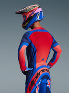 Vue de dos d'un pilote de motocross portant le maillot Alpinestars Supertech Vista 2026 en bleu marine foncé, corail éclatant et cobalt, avec un panneau arrière rouge vif et une construction sans couture, associé à un pantalon et un casque assortis pour un look de course complet.