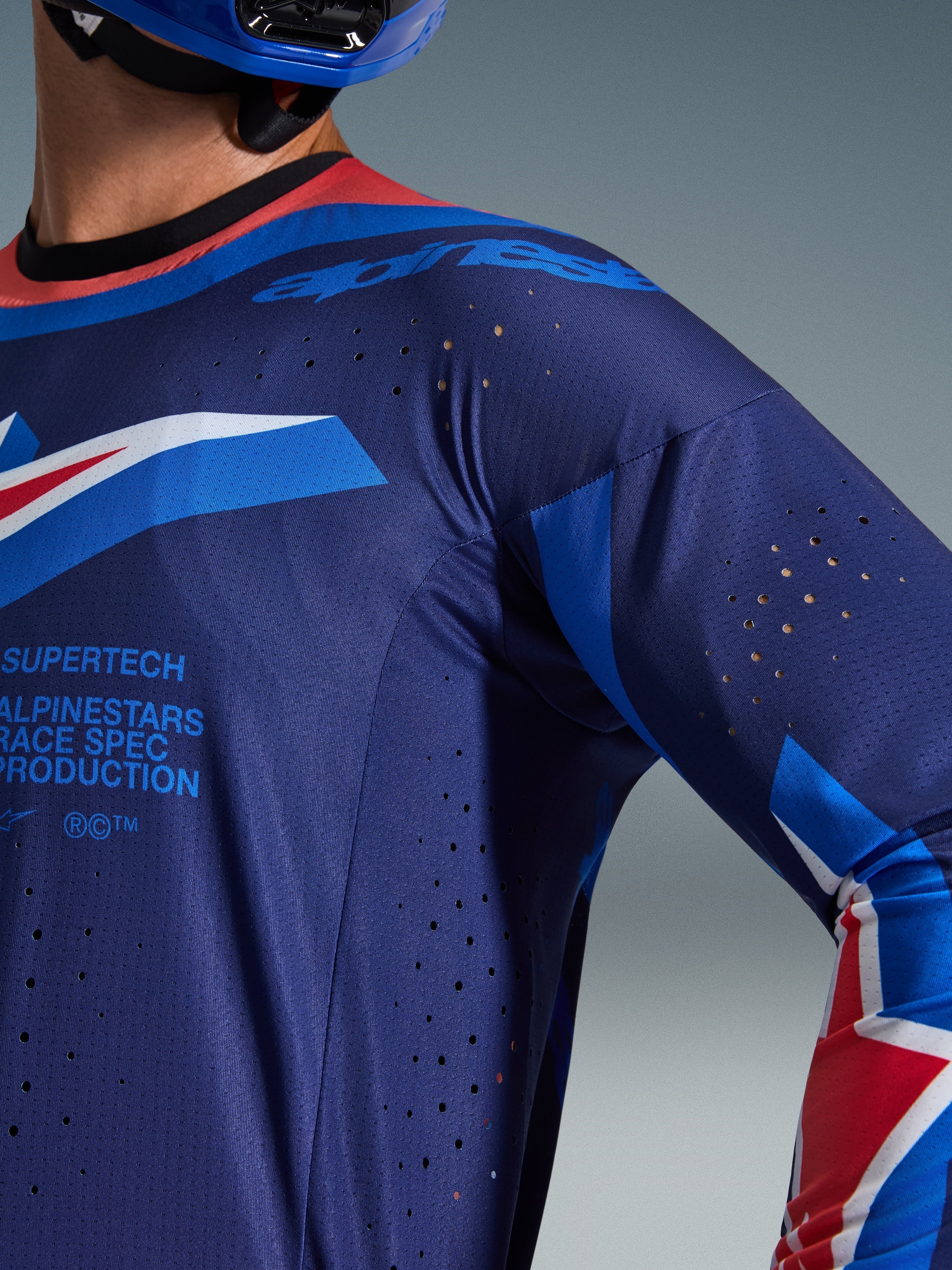 Maillot Alpinestars Supertech Vista 2026, gros plan sur le maillot bleu marine foncé et bleu cobalt avec col corail vif, perforations de ventilation découpées au laser et marquage Alpinestars Race Spec, construction en mesh athlétique haut de gamme pour le motocross