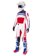 Pilote de motocross portant une tenue de course complète, comprenant le maillot Alpinestars Limited Edition Techstar Fortitude en rouge éclatant, blanc et bleu. Pantalon de motocross assorti, casque blanc avec lunettes bleues et bottes bleues et rouges, offrant un look coordonné pour la compétition tout-terrain.