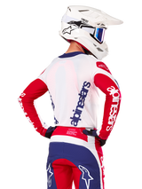 Maillot Alpinestars Limited Edition Techstar Fortitude, maillot de motocross, rouge vif, blanc et bleu, vue de dos d'un pilote portant un casque blanc et une tenue assortie, avec logos Alpinestars imposants sur le dos et les manches, conçu pour la course tout-terrain haute performance