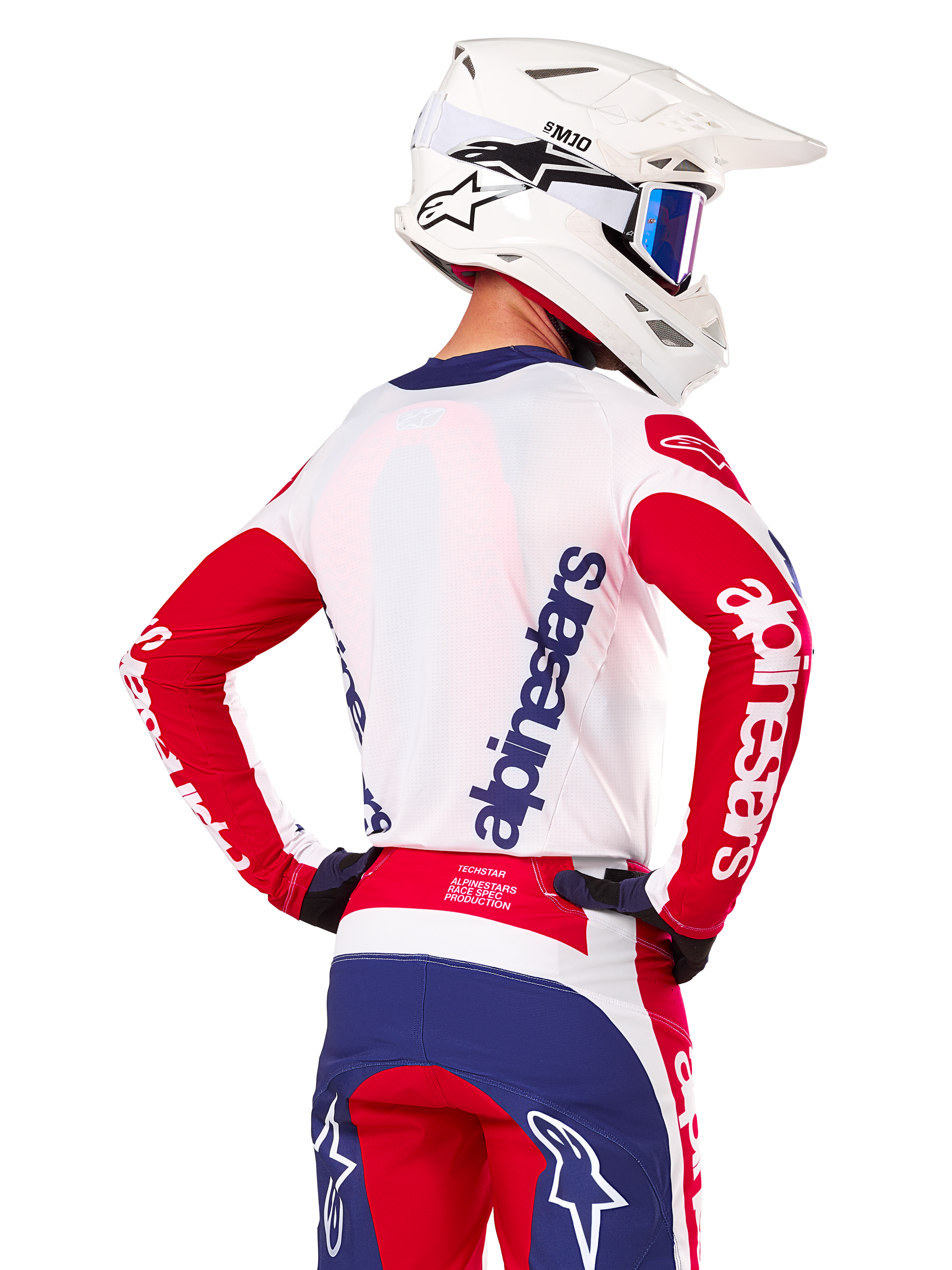 Maillot Alpinestars Limited Edition Techstar Fortitude, maillot de motocross, rouge vif, blanc et bleu, vue de dos d'un pilote portant un casque blanc et une tenue assortie, avec logos Alpinestars imposants sur le dos et les manches, conçu pour la course tout-terrain haute performance