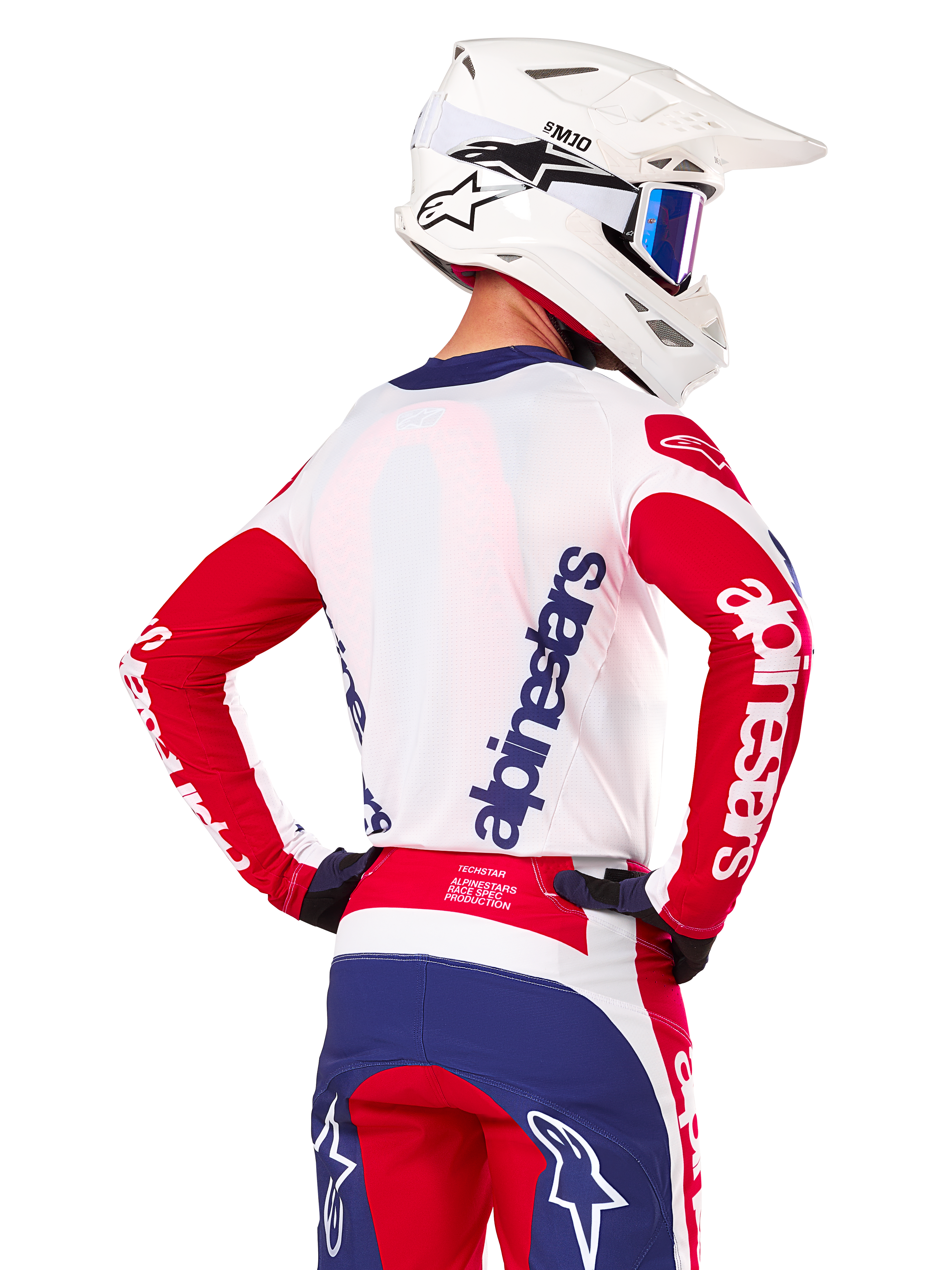 Maillot Alpinestars Limited Edition Techstar Fortitude, maillot de motocross, rouge vif, blanc et bleu, vue de dos d'un pilote portant un casque blanc et une tenue assortie, avec logos Alpinestars imposants sur le dos et les manches, conçu pour la course tout-terrain haute performance