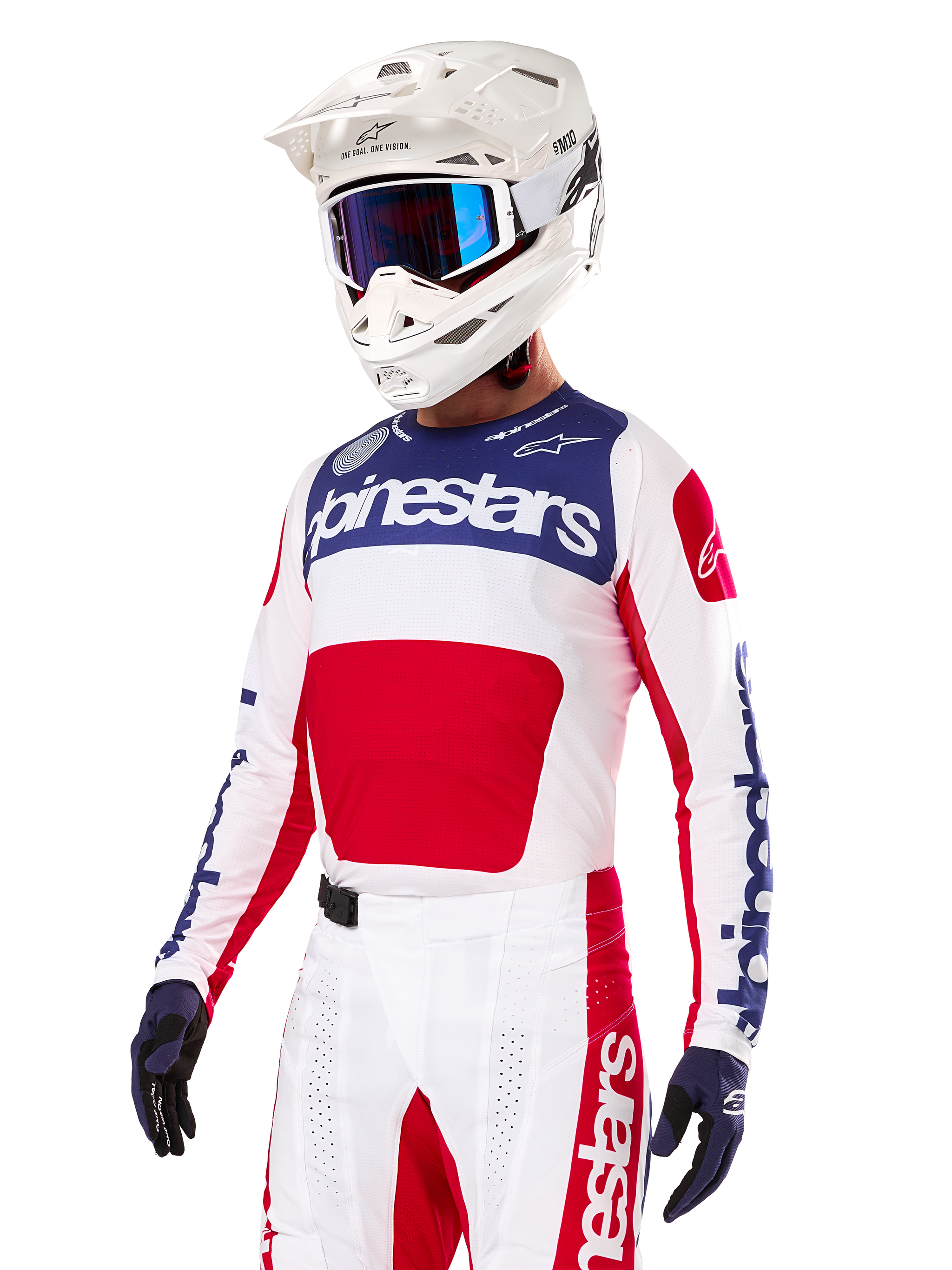 Pilote de motocross portant le maillot Alpinestars Limited Edition Techstar Fortitude, rouge vif, blanc et bleu, avec un casque blanc, des lunettes bleues et un pantalon assorti, équipement de course haute performance pour la compétition tout-terrain