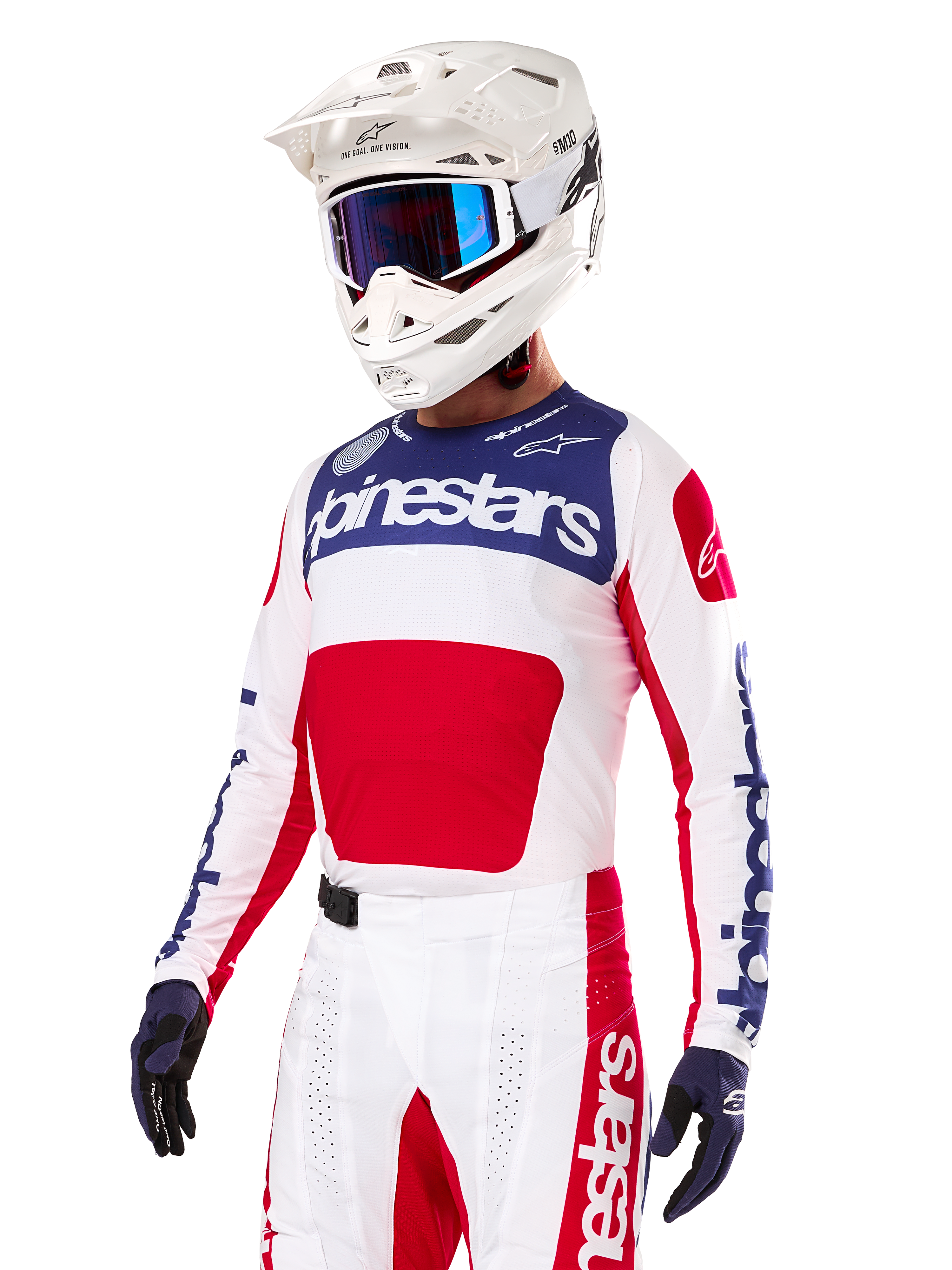 Pilote de motocross portant le maillot Alpinestars Limited Edition Techstar Fortitude, rouge vif, blanc et bleu, avec un casque blanc, des lunettes bleues et un pantalon assorti, équipement de course haute performance pour la compétition tout-terrain