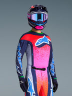 Alpinestars Limited Edition Supertech Records Jersey, Motocross jersey and matching gear, Multicolor with navy blue, pink, and orange splattered accents, large blue and white logo on chest, worn with coordinating helmet and gloves, athletic race-ready fit