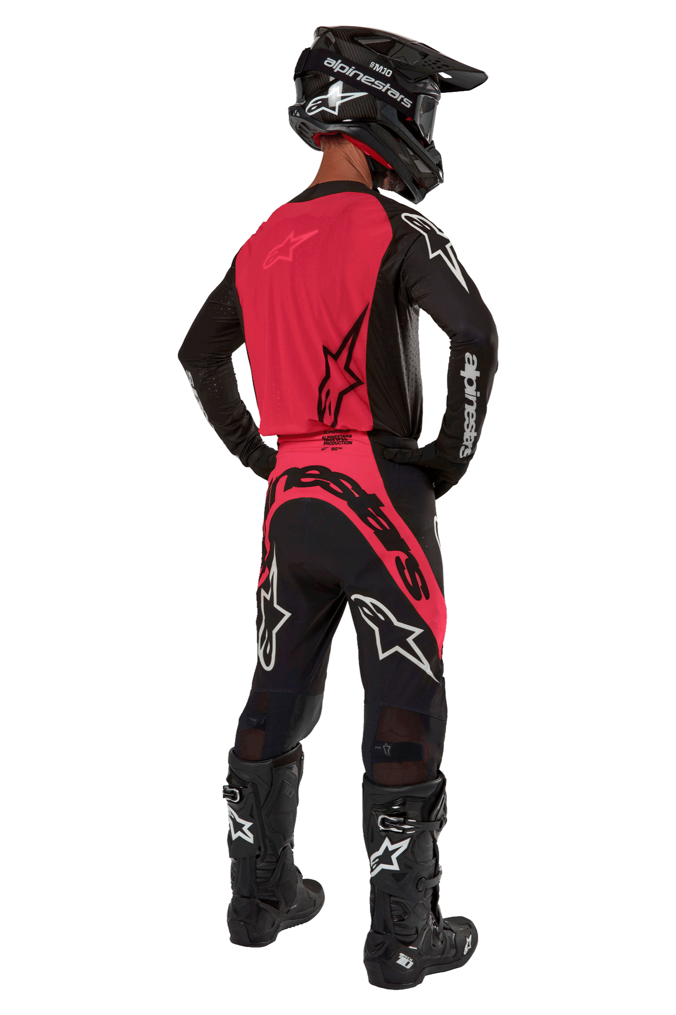 Pilote de motocross vu de derrière portant le maillot Alpinestars Supertech Ward 2024 en Black Red Berry, avec un panneau dorsal rouge vif et des manches noires, associé à un pantalon assorti, des bottes Tech 10 noires et un casque en fibre de carbone pour une tenue de course professionnelle.